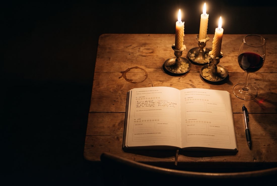 Das aufgeschlagene Buch bei Kerzenlicht auf einem Holztisch, eine Seite ist bereits handschriftlich ausgefüllt