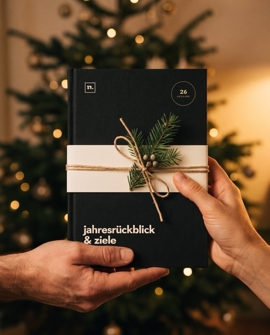 Genau zwei Hände halten das Buch mit Banderole und Tannenzweig vor dem Weihnachtsbaum